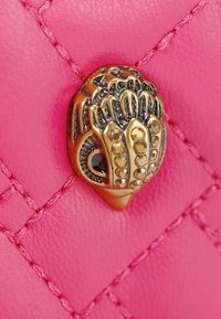 In pelle rosa con texture trapuntata, presenta una chiusura dettagliata in tono oro a forma di mano, adornata con pietre decorative e accenti.