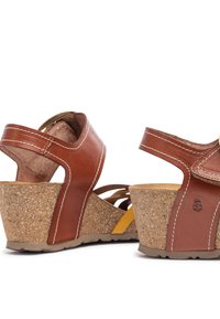 Bruine leren wedgesandalen met een kurken plateau. Beschikt over een breed bandontwerp en een contrasterende gele accent, textuurzool voor grip.