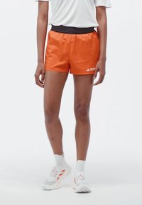 Oranžové športové šortky s elastickým čiernym pásom. Vyrobené z ľahkého materiálu, s logom umiestneným na spodnej strane.