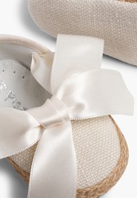 Crème-kleurige espadrilles met een textuurstof bovenkant, jute zool en een grote satijnen strik aan de voorkant.