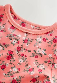 Cămașă lungă cu mâneci, roz corai, cu un model floral în roșu, alb și verde. Decolteu rotund cu margine zimțată. Țesătură din bumbac moale.