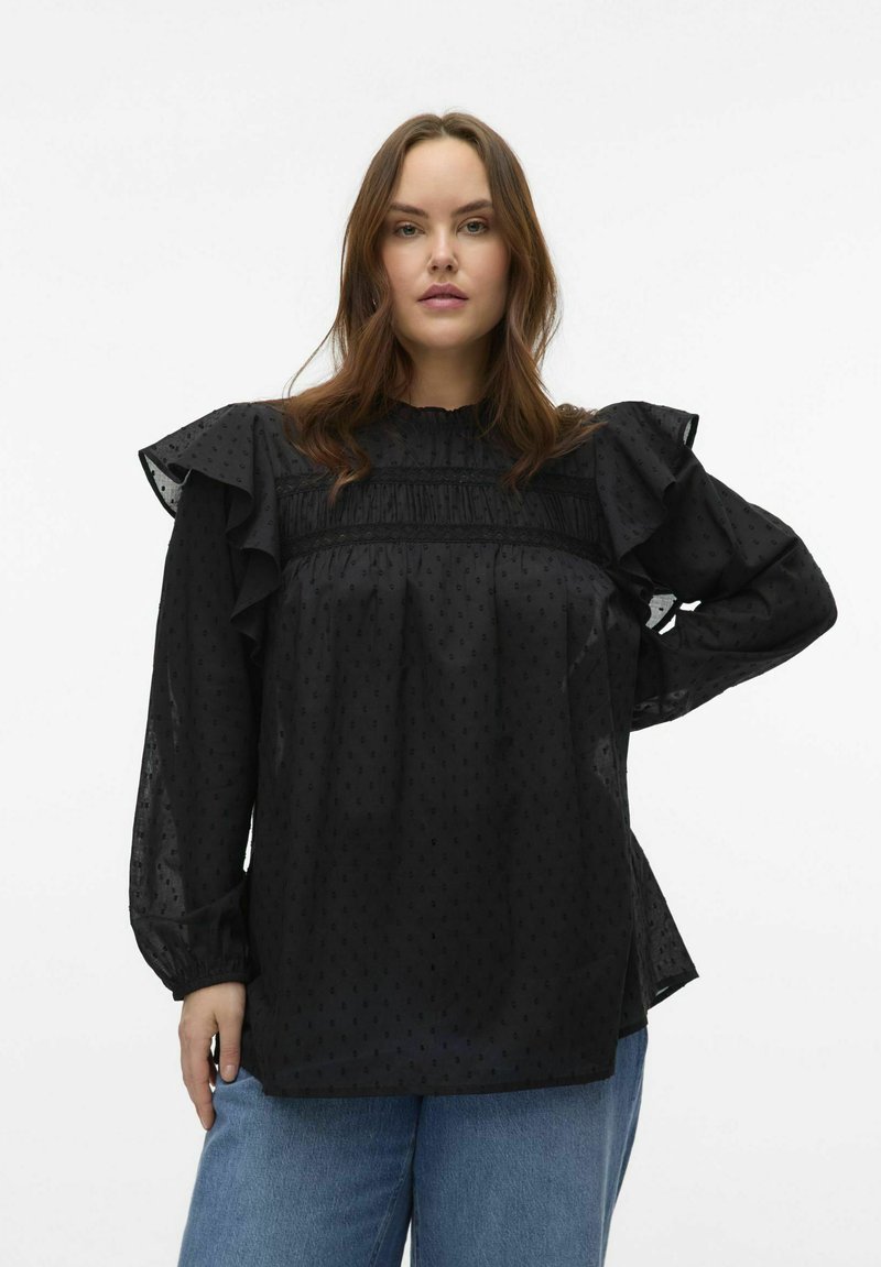 Blusa nera con texture semi-trasparente, maniche arricciate e scollo arricciato. Presenta pois tonali e una vestibilità morbida. Abbinata a jeans chiari.