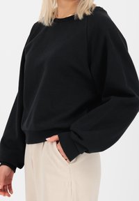 Mustat hupparit, jotka ovat rentoa istuvuutta, ribbed-hihansuut ja pyöreä kaula-aukko. Sileä kangas, pitkät hihat ja vyötäröosa, joka istuu lantion kohdalla.