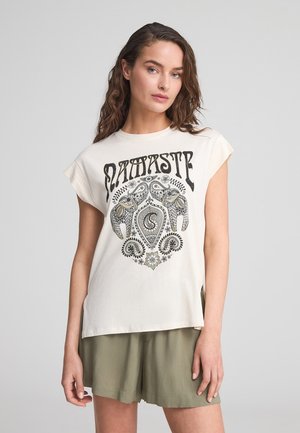 T-shirt in cotone color crema con un design grafico nero che presenta elefanti e motivi floreali. Le maniche a cappuccio e le fessure laterali aggiungono dettagli.