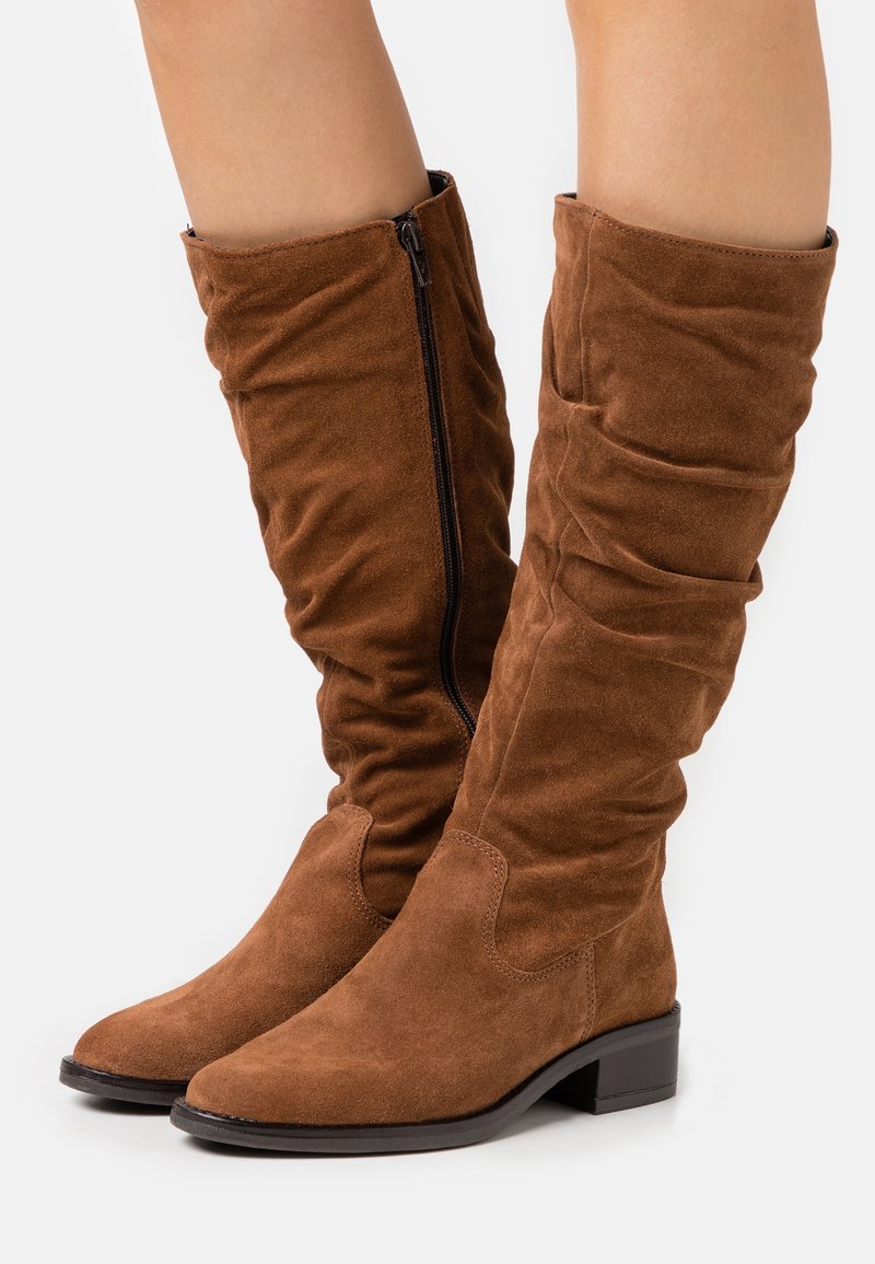 Bottes hauteur genou en daim marron avec un design à effet froissé, dotées d'une fermeture éclair latérale et d'un petit talon bloc. Texture lisse et bout pointu.