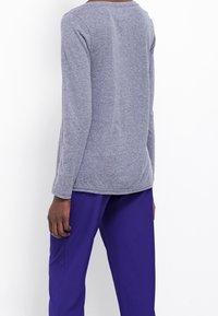 Grå långärmad topp med rund halsringning och mjukt tyg. Kombinerad med livfulla lila byxor som visar en avslappnad passform och casual stil.