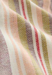 Tissu tissé avec des rayures horizontales texturées dans des couleurs sourdes comprenant olive, rouge, pêche et crème, présenté avec de doux plis.