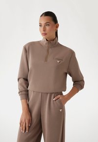 Beige zip-up sweatshirt med høj krave, frontlomme og pyntede logo detaljer. Glat stof med ribbede manchetter og kant.