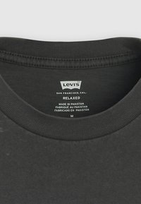 T-shirt nera in cotone con collo a costine. L'etichetta mostra "Levi's", taglia M, istruzioni per la cura e "Made in Pakistan". Design semplice.