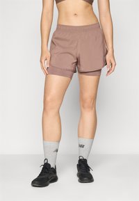 Shorts de sport marron avec une taille élastique, conçus pour le confort et la mobilité. Associés à des chaussettes grises et des baskets noires.