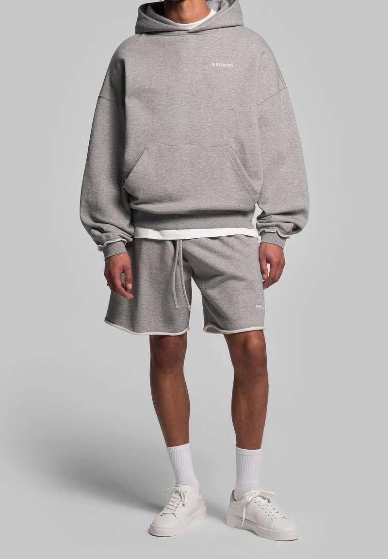 Personne portant un sweat à capuche gris avec poche avant et short gris assorti avec cordon, chaussettes blanches et baskets blanches.