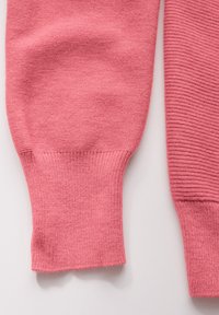 Manchons de pull en tricot rose à texture côtelée. Un manchon est lisse tandis que l'autre présente un motif côtelé horizontal. Finition en tissu doux.