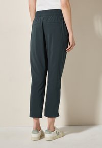 Pantalons vert foncé, mi-mollet, avec une taille élastique, deux poches arrière et une texture lisse, associés à des baskets blanches.