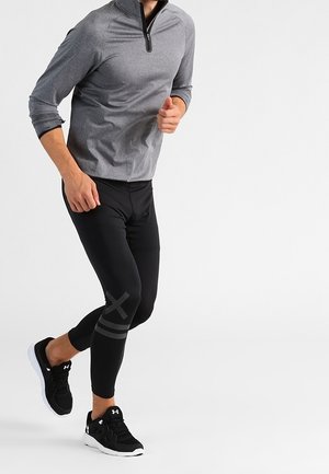 Szara sportowa koszulka z długim rękawem i ćwierć zamkiem, zestawiona z czarnymi dopasowanymi legginsami z szarymi akcentami oraz czarnymi butami sportowymi.