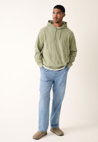 Felpa con cappuccio verde oliva con motivo a diamante testurizzato, cappuccio con coulisse, abbinata a jeans azzurri e scarpe slip-on beige.