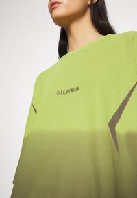 Světlezelená síťovaná mikina s hnědými akcenty. Má kulatý výstřih a logo text na přední straně. Texturovaný vzor na látce.