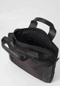 Μαύρη νάιλον τσάντα με δερμάτινες λεπτομέρειες, διπλούς χειρολισθήρες και πάνω φερμουάρ. Ο εσωτερικός χώρος διαθέτει μια τσέπη με φερμουάρ και επένδυση από υφασμάτινη υφή.