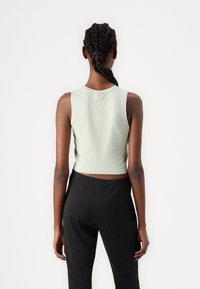 Svetlo zelena skrajšana majica brez rokavov z okroglim izrezom, v kombinaciji s črnimi hlačami, prikazana od zadaj. Mehka bombažna tkanina.