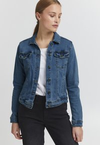 Denim jakna v srednje modri barvi, s sprednjim zapenjanjem na gumbe, dvema žepoma na prsih in krajšim krojem, klasičnim ovratnikom in dolgimi rokavi.