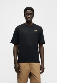 Μαύρο βαμβακερό T-shirt με κοντά μανίκια, με μικρό χρυσό λογότυπο στο αριστερό στήθος. Διαθέτει χαλαρή εφαρμογή και στρογγυλή λαιμόκοψη.