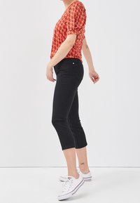 Blouse florale rouge à manches bouffantes, pantalon noir court et baskets blanches. La blouse présente un motif ; le pantalon est ajusté avec des poches.