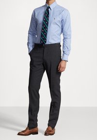 Camisa de vestir a rayas azul claro y blanca, pantalones oscuros gris, corbata de punto con acentos y patrones verdes, zapatos de cuero marrón. Corte ajustado.