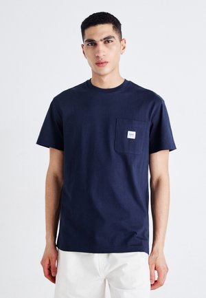 T-shirt di cotone blu navy con maniche corte, colletto a girocollo e dettaglio della tasca sul lato sinistro del petto con una toppa del logo bianca.