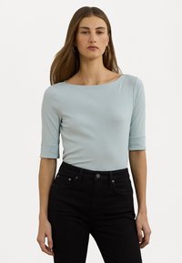 Haut ajusté bleu clair avec un décolleté bateau et des manches trois-quarts. Fabriqué en tissu lisse, associé à un jean noir taille haute.