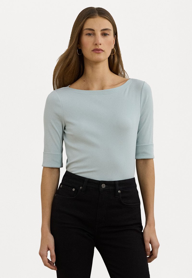 Haut ajusté bleu clair avec un décolleté bateau et des manches trois-quarts. Fabriqué en tissu lisse, associé à un jean noir taille haute.