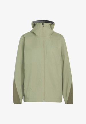 Kvinde iført lys grøn hættetrøje, sorte bukser og beige sneakers gående mod en ensfarvet lys baggrund.