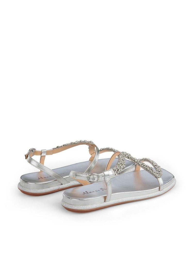 Sandalias planas plateadas con un acabado metálico suave, que presentan acentos decorativos de strass en las correas y un cierre de hebilla.