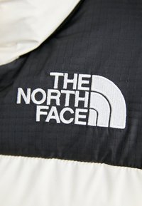 Fekete-fehér szövetdzseki "THE NORTH FACE" logóval. Fekete, struktúrált rácsos minta, sima fehér hangsúly az alján.