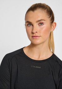 Czarna, długorękawowa koszulka sportowa z okrągłym dekoltem i subtelną teksturą. Zawiera szare logo "hummel" na klatce piersiowej.