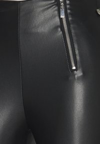 Svarta leggings i konstläder med en slät yta, en figurnära design och en dekorativ silverdragkedja på sidan.