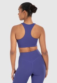 Paarse sportbeha met een racerback-ontwerp, een gladde textuur en een ondersteunende band. Gecombineerd met bijpassende hoge taille legging.