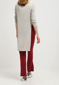 Gray ribbed long-sleeve cardigan with a high-low hem, paired with fitted burgundy pants and white sneakers with a gray pattern.
