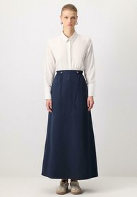 Navy maxi skirt with a drawstring waist, featuring silver hardware and a smooth texture, paired with a white button-up shirt and beige sneakers.