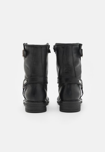 Botines de cuero negro hasta el tobillo con un tacón bajo, que presentan detalles de hebillas y costuras en la parte trasera. Textura suave y diseño minimalista.