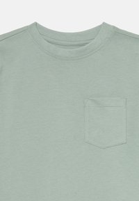 T-shirt vert clair à manches courtes en coton doux, avec un col rond et une poche poitrine rectangulaire avec un détail de couture.