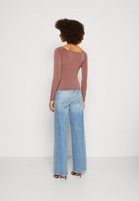 Langärmliges Oberteil aus mauvefarbenem Stoff mit weitem Ausschnitt, kombiniert mit hellblauen weit geschnittenen Jeans und hohen Schuhen, von hinten betrachtet.