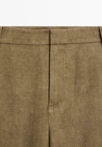 Pantaloni verde oliva realizzati in un tessuto morbido e testurizzato, con vita alta e dettagli di cucitura, dal design pulito e senza tasche visibili.