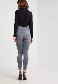 Leggings gris de tiro alto con un diseño ajustado, que presentan bolsillos traseros y detalle de costura decorativa, combinados con tacones altos negros.