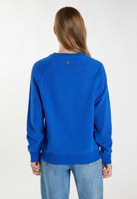 Blauwe sweatshirt met een geribbelde halslijn en manchetten, featuring een klein logo op de achterkant. Soepele textuur, losvallende pasvorm, gecombineerd met denim jeans.