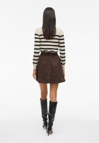 Pulover z črtami v kremni in črni barvi, kombiniran z mini krilom iz rjavega semiša. Model nosi visoke črne škornje z visoko peto. Celotna tekstura je gladka.