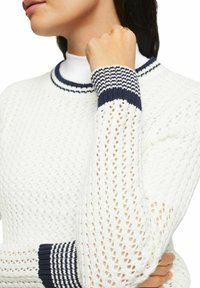 Weiße Strickjacke mit strukturiertem Muster, ausgestattet mit navy gestreiftem Rippkragen und -bündchen sowie langen Ärmeln mit offenem Gewebe.