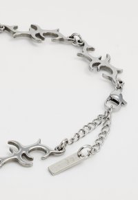 Silver metal bracelet with interlocking ornate shapes and a lobster clasp with an adjustable chain on a white background.