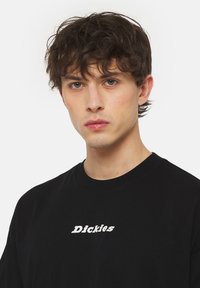 Černé bavlněné tričko s kulatým výstřihem a krátkými rukávy, s bílým potiskem "Dickies" na přední straně. Jednoduchý design, volný střih.