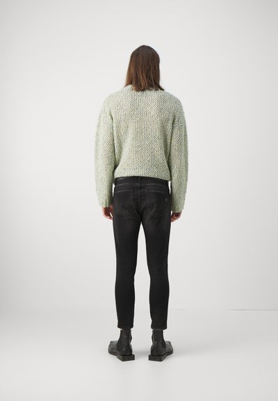 Maglione a maglia verde chiaro con texture, maniche lunghe, abbinato a jeans neri slim e stivali neri alla caviglia, vista da dietro.