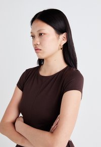 Brown short-sleeve dress with a fitted design, made from a smooth fabric. Features a round neckline and minimal stitching details.