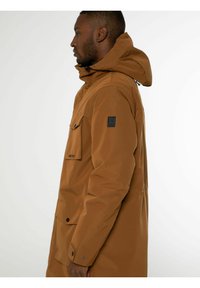 Parka imperméable marron avec capuche, dotée d'une fermeture éclair, de deux poches avant et d'un patch logo sur la manche. Matière lisse et durable.